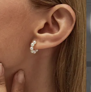 Detail von 18K Gold-Edelstahl-Ohrringen mit eleganten weißen runden Perlen am Ohr