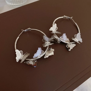 Detail of silver butterfly hoop earrings with etched textures on a textured surface