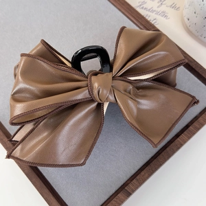 Detail shot of a brown vintage leather bow hair claw clip with dark brown piping edges