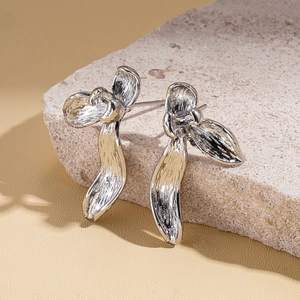 Macro shot of silver textured petal earrings displayed on a natural light stone surface