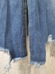 Close-up of denim skirt hem featuring double yellow stitching and distressed fringe details