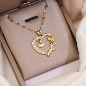 Close-up of gold heart necklace with rose flower detail and small charm in a jewelry box