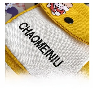 Detail of yellow canvas bag featuring black embroidered lettering and a cute cartoon brooch