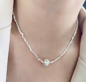 Close-up of silver beaded necklace with round metal pendant on a white suit jacket