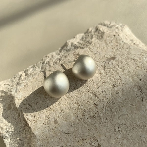 Close-up of matte champagne bean-shaped earrings on a textured natural stone surface