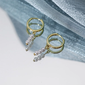 Close-up of elegant gold pearl drop earrings with glossy reflection on a soft blue background