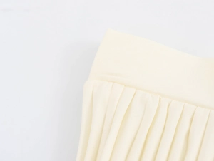 Detailed close-up of pale yellow pleated skirt waistband and fine fabric texture