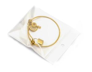 Detailed close-up of golden coil bracelet with rhinestone key and padlock charms in packaging