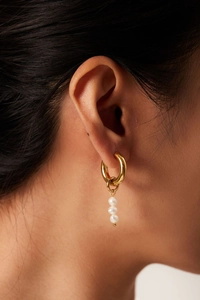 Close-up of asymmetrical gold stainless steel hoop earrings with natural freshwater pearls