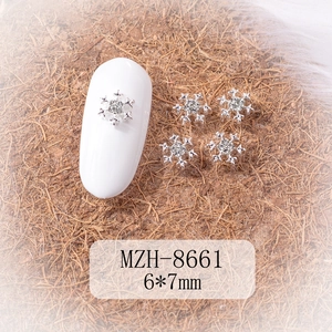 Macro shot of silver 6x7mm snowflake nail charms with glittery rhinestones on a nail tip