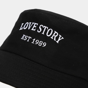 Detail view of white LOVE STORY embroidery on a premium black cotton fisherman bucket hat