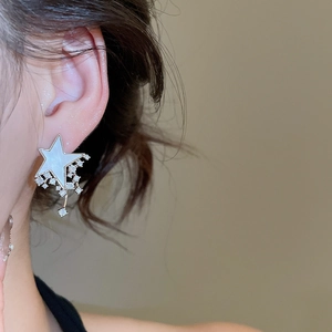 Close-up of sparkling star-shaped earrings with zircon tassels worn on a model's ear