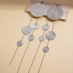 Macro detail of silver tiered disc tassel earrings on a textured stone surface