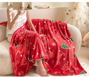 Cosy red Christmas flannel blanket with festive motifs draped over a woman on a sofa