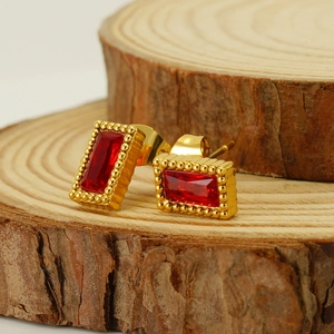 Boucles d'oreilles rectangulaires dorées avec zircons rouges sur fond de bois naturel