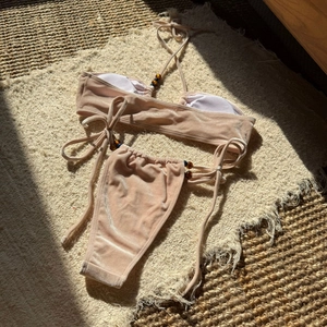 Flat lay of pink velvet bikini with metallic sheen and bead details on a woven rug