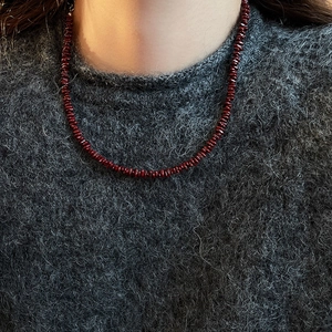 Macro shot of dark red crushed stone beaded necklace worn on a grey cashmere sweater