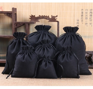 Multiple sizes of black drawstring cotton canvas jewelry pouches on a wooden shelf