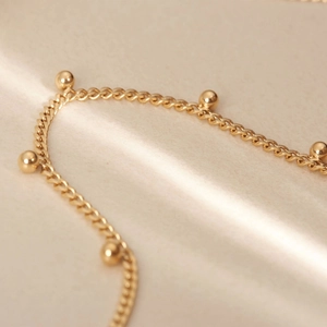 Macro detail of 18K gold plated stainless steel bead chain with polished metallic texture