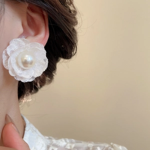 Dettaglio dell'orecchino a fiore con petali in pizzo bianco e perla sull'orecchio