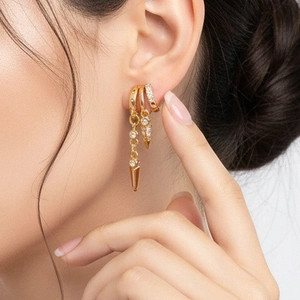 Close-up of gold tassel hoop earrings set with zircons and rivets on a female ear