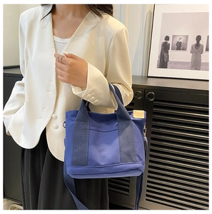 Blue canvas tote bag with adjustable shoulder strap and leather tag shown with model