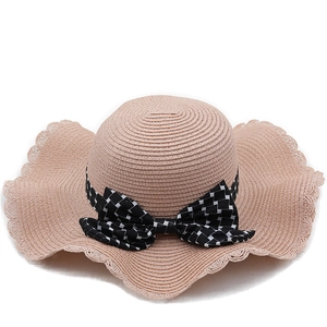 Detalle de sombrero de paja rosa con ala ondulada, encaje de ganchillo y lazo de cuadros