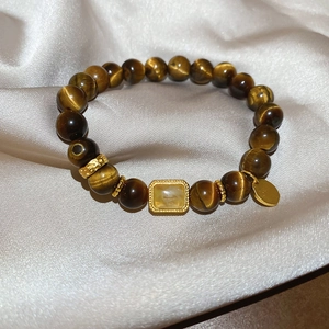 Handmade tiger eye bead bracelet with golden hollow square pendant on silk background