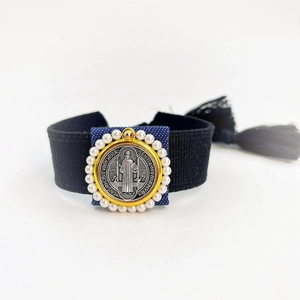 Macro shot of Saint Benedict medal with blue fabric and pearls on woven wristband