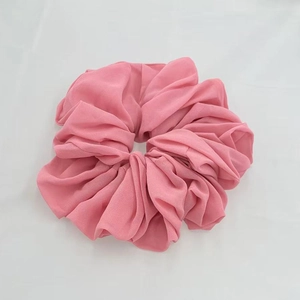 Macro detail of a large pink chiffon scrunchie with soft elastic pleated fabric texture