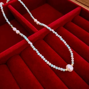 Détail d'un collier en amazonite et perle dans un coffret à bijoux en velours rouge