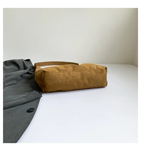 Detail shot of brown frosted suede tote bag lying on a surface next to a grey coat