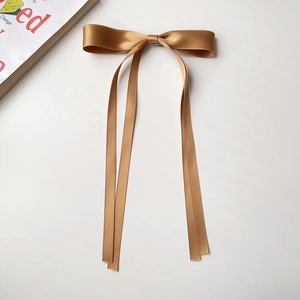 Detail view of large brown satin ribbon bow hair clip on a minimalist white surface