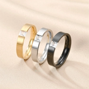 Close-up of three brushed titanium steel rings with square zircon in gold, silver, and black