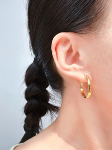 Nahaufnahme eines Models mit goldfarbenen, unregelmäßigen Creolen mit strukturierter Optik