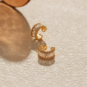 Close-up of gold-plated C-shaped ear cuffs with baguette-cut zircon and beaded edges