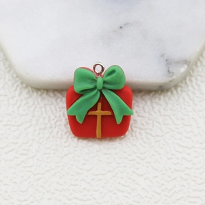 Macro view of red Christmas gift box charm with green bow and golden cross detail