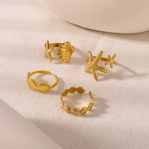 Close-up of four gold adjustable starfish and seashell rings on a textured fabric