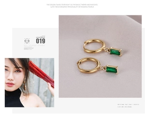 Detail of gold hoop earrings with rectangular emerald green gemstone charms on a model