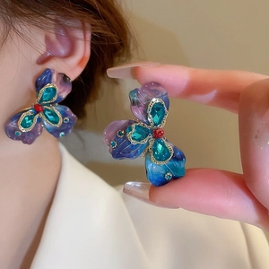 Detailed close-up of a large flower earring with purple resin petals and green crystal center