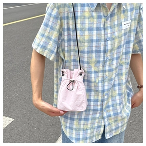 Detailed view of light pink nylon bucket bag with black drawstring closure and slim strap
