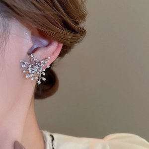 Detailed view of silver zircon and pearl firework stud earrings on a model's ear