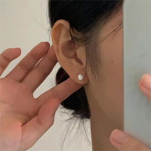 Close-up of a minimalist silver smiley face stud earring worn on the earlobe