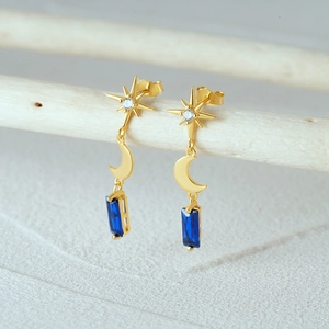 Macro view of gold star and crescent moon earring with deep blue gemstone on white branch
