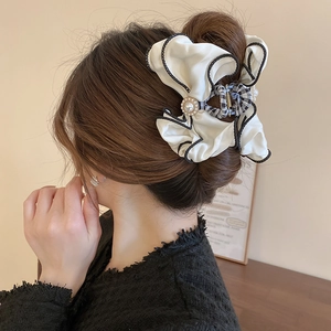 Detail of cream fabric bow hair claw with pearl accent and black wavy edge stitching
