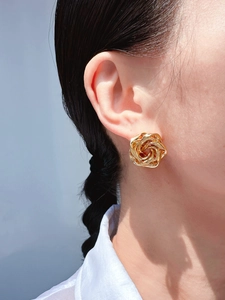 Detailed close-up of a golden irregular flower stud earring worn on a model's ear