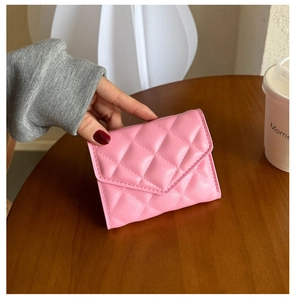Close-up of a pink quilted PU leather wallet held over a wooden table setting
