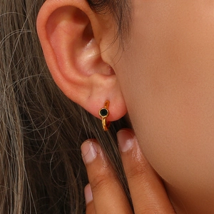 Close-up of a gold geometric earring with a deep green gemstone inlay on a person