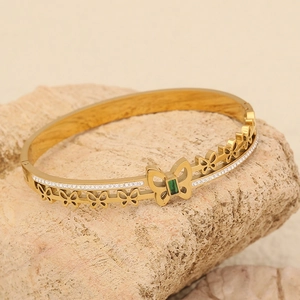 Detailed shot of golden butterfly bangle with green gemstone on a natural stone base