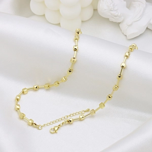 Collana bicolore stile bambù con perline dorate su sfondo di raso bianco lucido